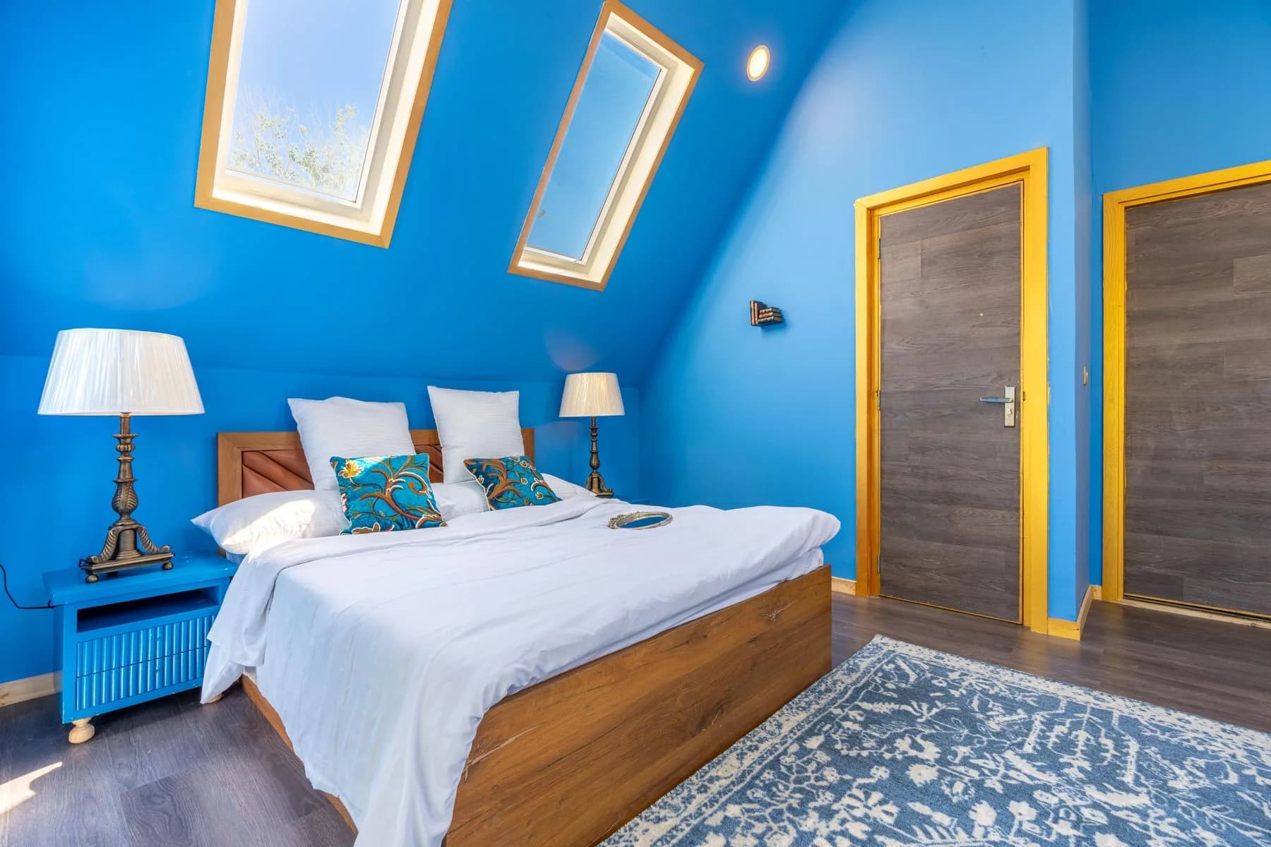 Blue loft bedroom with two roof windows above a wooden bed — design inspiration